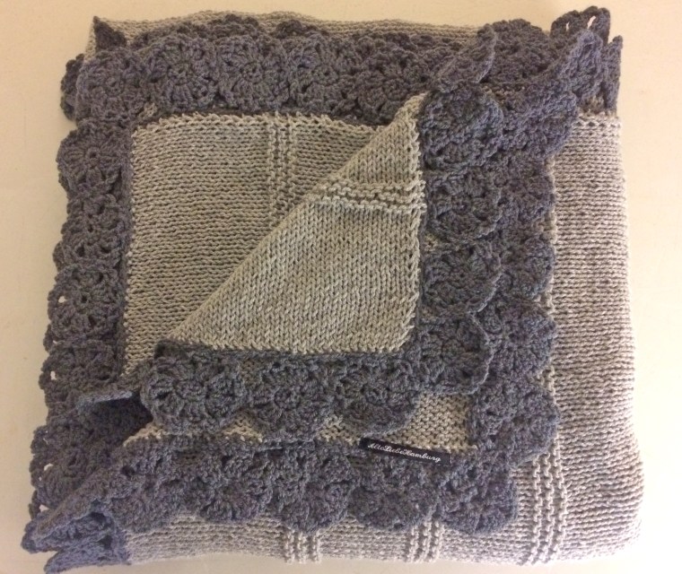 Strickdecke in hellgrau mit dunkelgrauen Häkelblüten