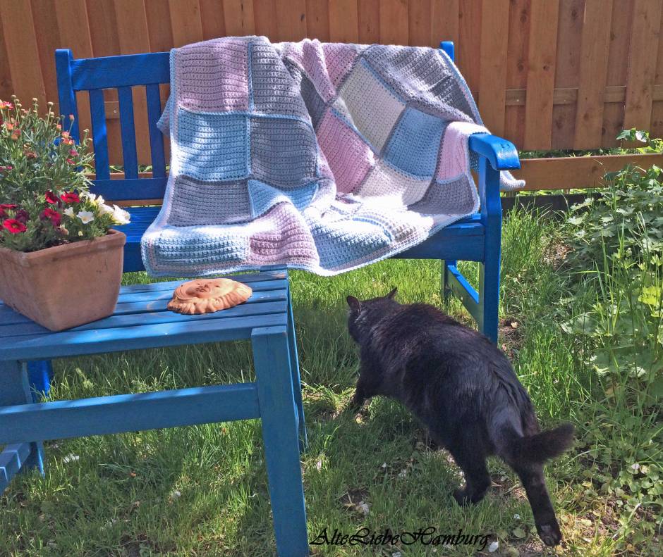 Tagesdecke Granny square in rose, blau, grau und weiß gehäkelt auf einer blauen gartenbank