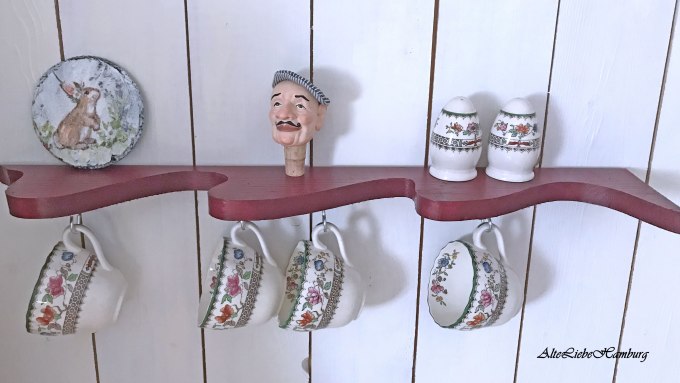 Rotes Wandregal aus Holz an dem Tassen hängen.