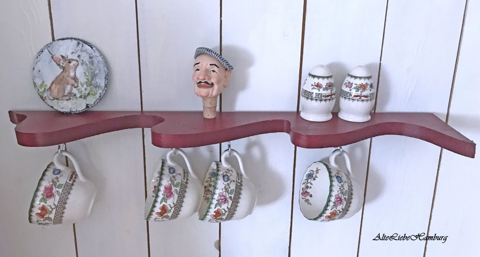 Rotes Wandregal aus Holz an dem Tassen hängen.