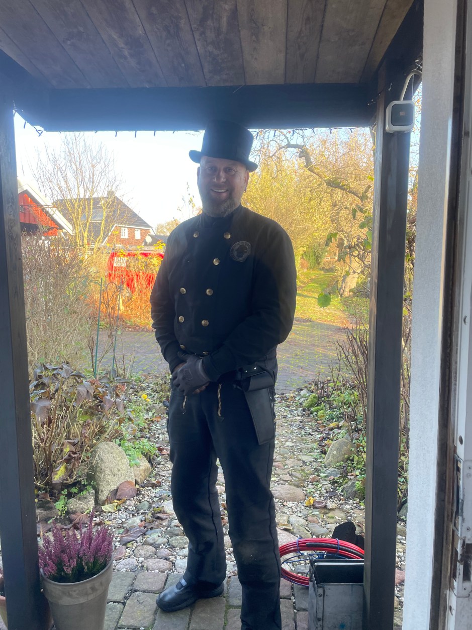 ein schornsteinferger steht vor der tür und sieht freundlich in die kamera