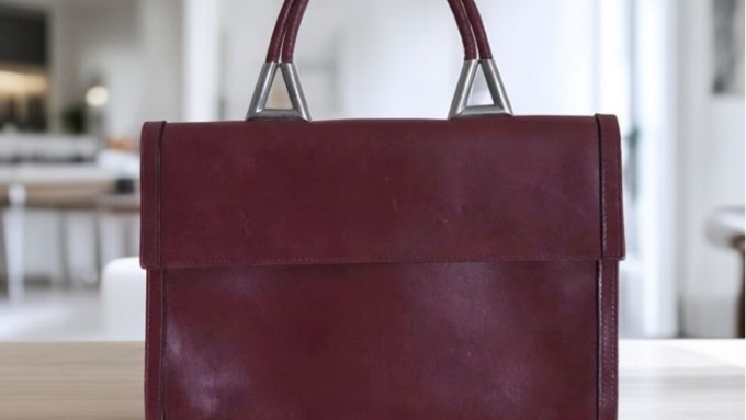 Dunkelrote Lederhandtasche mit Henkel steht auf einem modernen Tisch