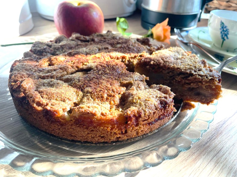 Fertig gebackener gedeckter Apfelkuchen, angeschnitten, mit Apfel und Rose dekoriert