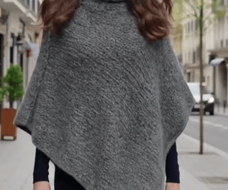 Eine junge Frau trägt einen handgestrickten grauen Poncho aus Lopi-Wolle